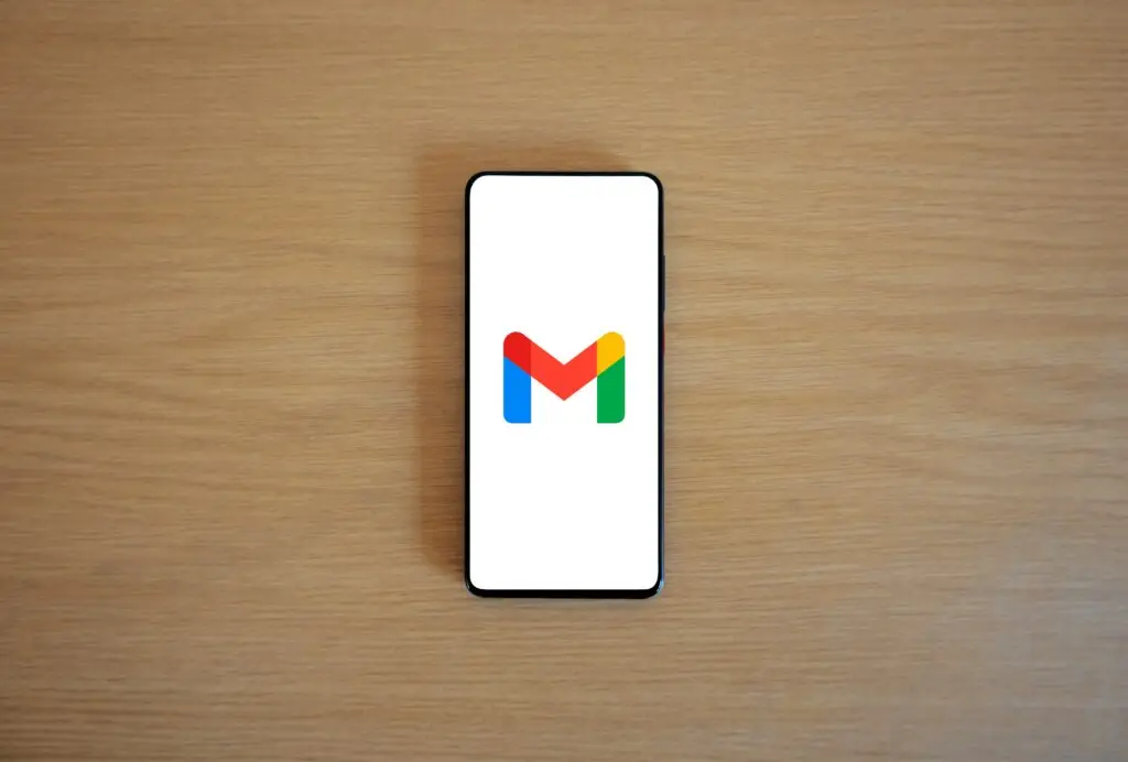A smartphone displaying the Gmail app logo on a wooden surface, viewed from above.