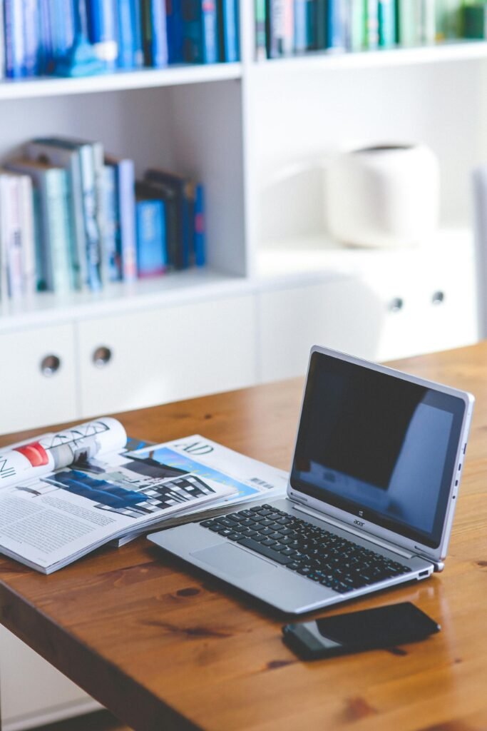 A stylish desk setup featuring a laptop, magazine, and bookshelf in a contemporary home office.